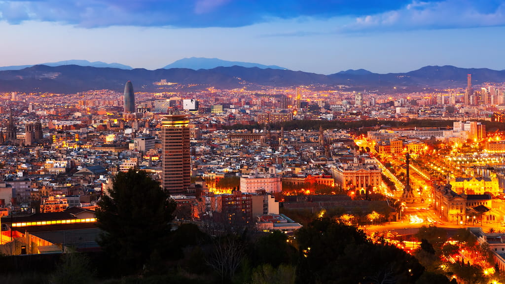 Vista panorĆ”mica del crepĆŗsculo en Barcelona, utilizada para ilustrar la investigación del BeeGroup de CIMNE. El paisaje urbano brilla con las luces de las calles y la iluminación de los edificios, destacando la densidad urbana y las infraestructuras. La Torre Glòries se destaca como un hito moderno dentro de la cuadrĆcula del Eixample. La imagen evoca temas centrales en el trabajo de BeeGroupāciudades energĆ©ticamente eficientes, tecnologĆas inteligentes para edificios y soluciones ambientales basadas en datosāenmarcadas por la silueta natural de las montaƱas circundantes.