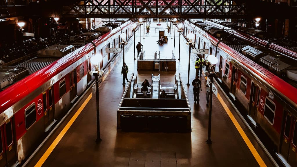 FotografĆa de una concurrida estación de tren urbano utilizada para ilustrar las capacidades de la Unidad de Innovación en Transporte CENIT de CIMNE. Dos trenes rojos flanquean una plataforma central donde la gente camina y espera. Las escaleras mecĆ”nicas descienden a un nivel inferior, y una pasarela peatonal con estructura de celosĆa se ve en la parte superior. La estación estĆ” bien iluminada con seƱalización y elementos de infraestructura que resaltan la dinĆ”mica del transporte pĆŗblico, el flujo de pasajeros y la conectividad multimodalātemas centrales en la investigación en movilidad y logĆstica de CENIT.