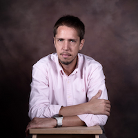 A professional portrait of Carles Estruch, a Tech Transfer & Innovation Senior Manager, wearing a light pink dress shirt, arms crossed, with a focused expression.