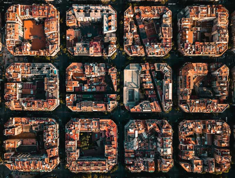 Aerial view of twelve blocks in Barcelona’s Eixample district, featuring chamfered corners, red-tiled roofs, and a central block with modern architecture and open space.