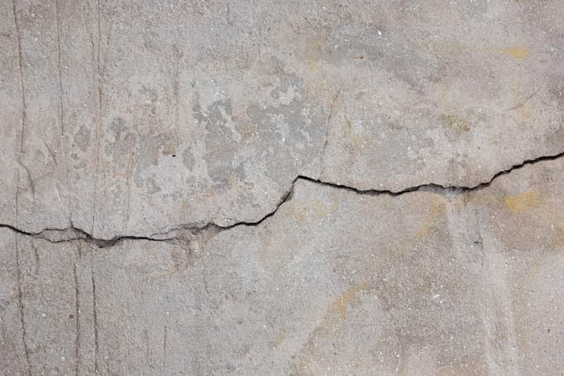Close-up of a rough concrete surface with a horizontal crack running across it, showing irregular width and surface discoloration.