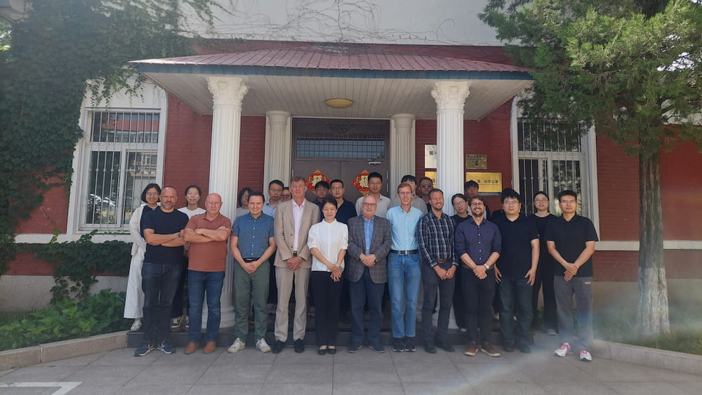 Representatives from CIMNE and BIAM pose for a group photo outside the BIAM headquarters in Beijing, standing in front of a red‑brick building with white columns and a roofed entrance.