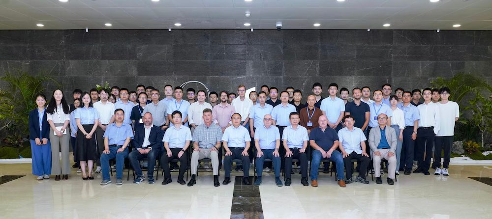 Representatives from CIMNE and CAE pose for a group photo inside the CAE headquarters in Beijing, seated and standing in a large lobby with marble flooring, potted plants, and a dark stone wall in the background.