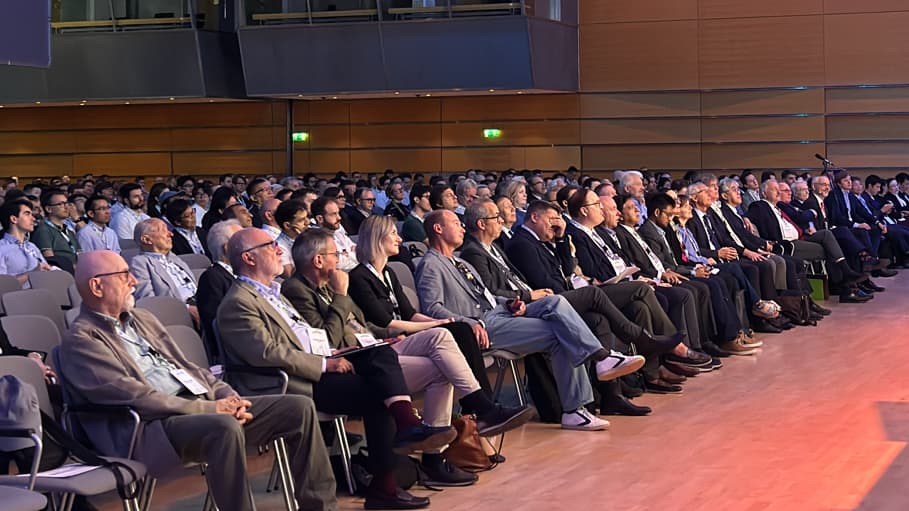 Audience members sit in rows inside a modern conference hall, attentively listening to a presentation. The room features wooden wall panels, overhead lighting, and a professional atmosphere suitable for a formal congress session.